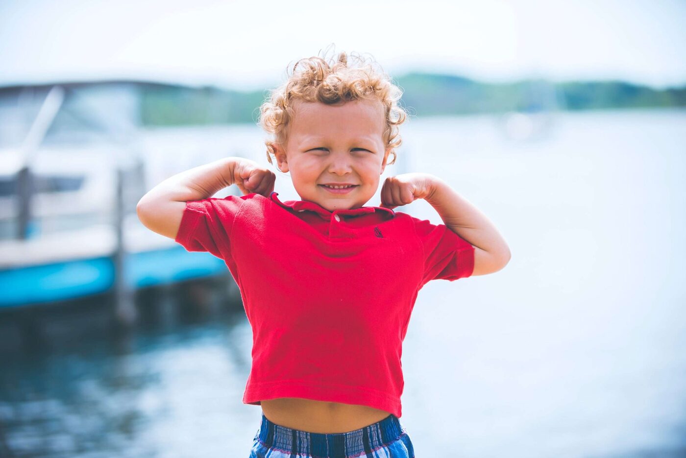 A small boy flexing his arms by the water on a sunny weekend